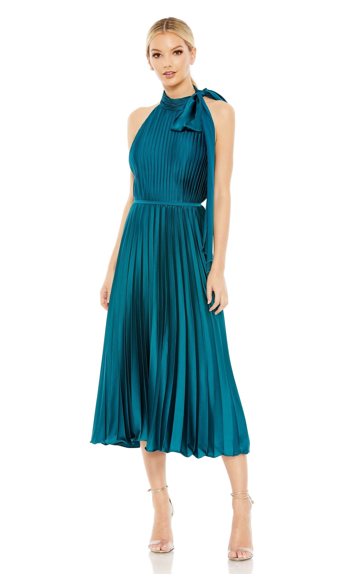 A woman wears the Tea Length Formal Dress 26909 by Mac Duggal, featuring a teal hue, pleats, high neck with bow detail, and pairs it with strappy nude heels.